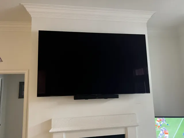 A TV and soundbar mounted on the drywall chimney breast above a white mantel