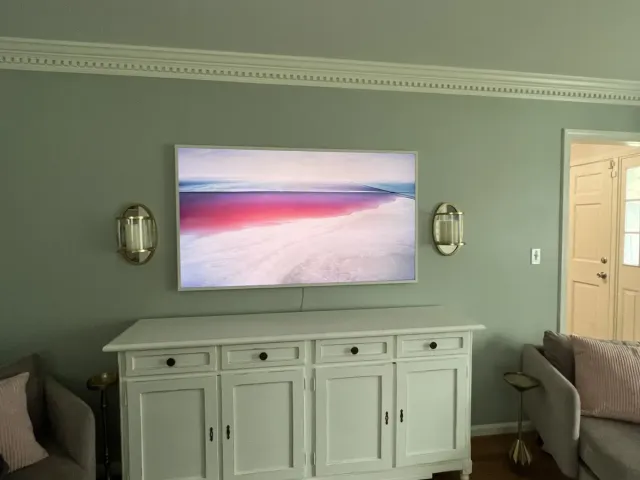 A TV on a flat mount centered above a white dresser on a sage-green bedroom wall