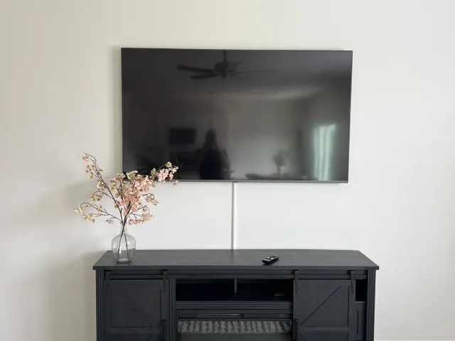 A TV on a flat mount on a white wall next to a black media cabinet