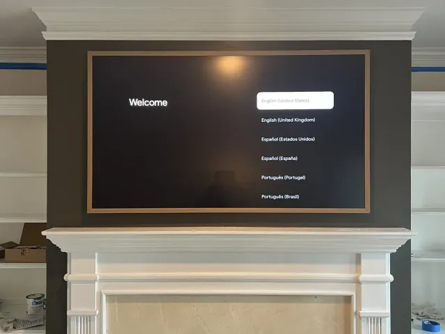 A Samsung Frame TV with a bronze bezel in a dark-painted alcove above a white mantel and marble surround, built-ins on both sides