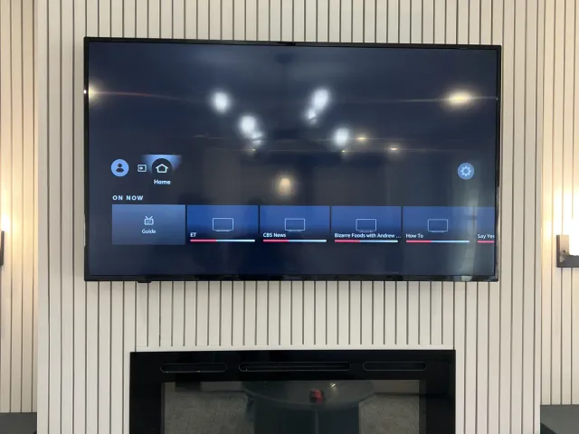 A TV mounted on a vertical slat accent wall above a linear electric fireplace