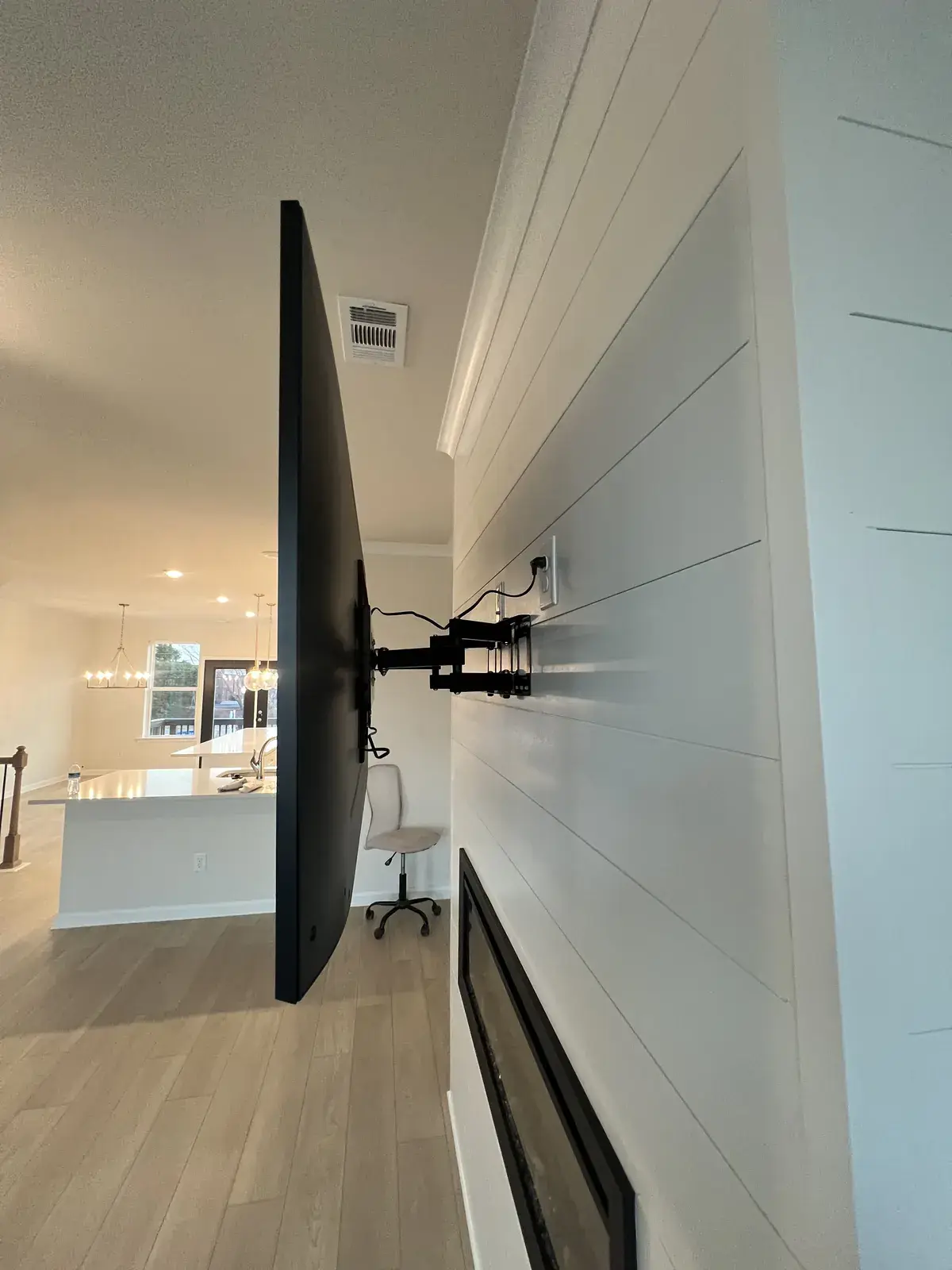 Side view of the same TV on its full-motion arm, showing the shiplap wall and an open kitchen behind