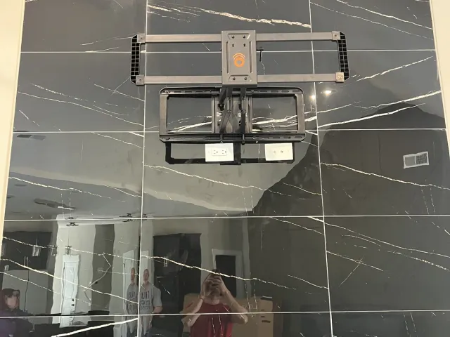 A full-motion wall plate and arm installed on a black marble-look porcelain tile fireplace wall