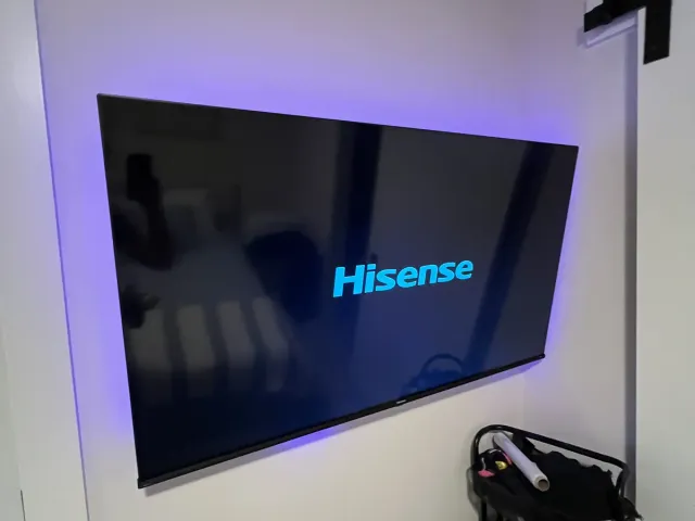 A Hisense TV on a white wall with purple LED bias lighting glowing behind it