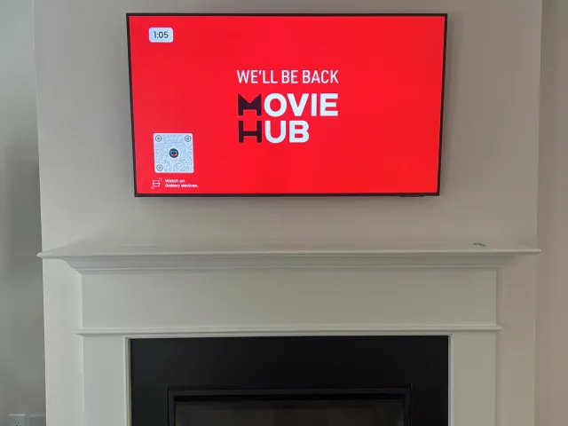 A TV mounted on the drywall above a white mantel with a black firebox