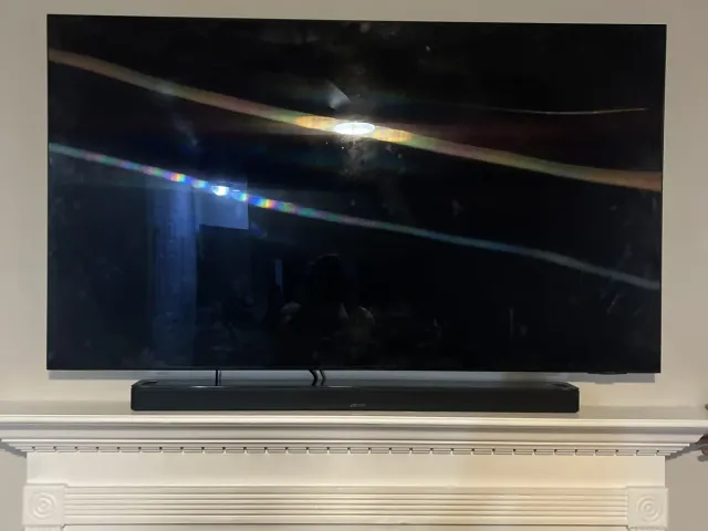 A TV with a soundbar beneath it mounted above a white mantel fireplace