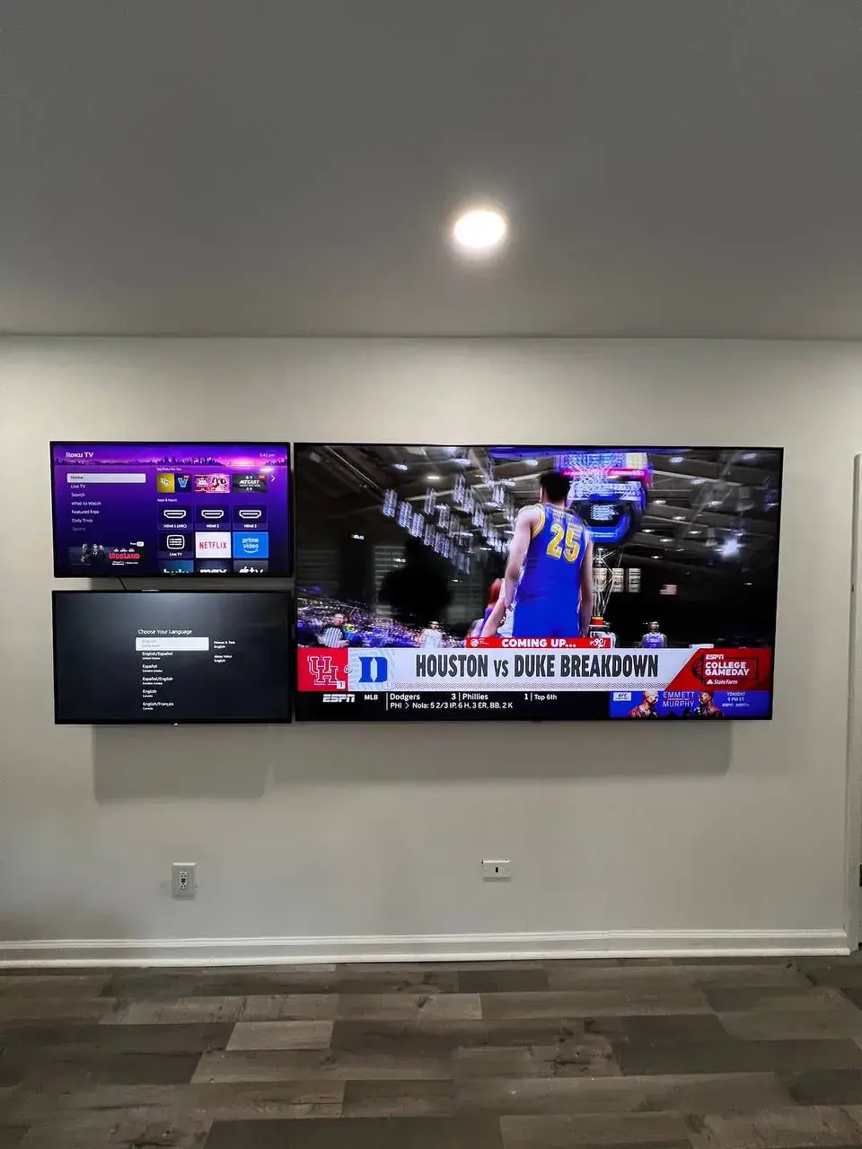 Two TVs mounted side by side on a gray basement wall over a wood-look floor