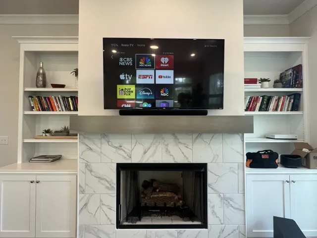 A TV and soundbar above a marble-tile fireplace flanked by white built-in bookshelves