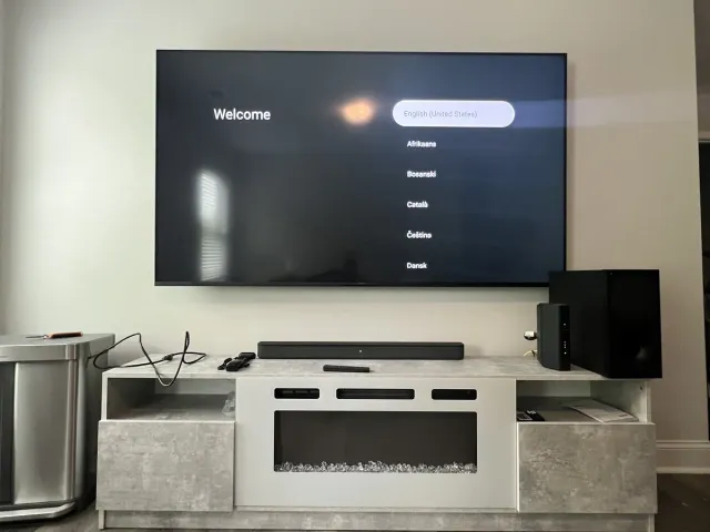 A TV on a white wall above a white console holding a sound system, showing its welcome screen
