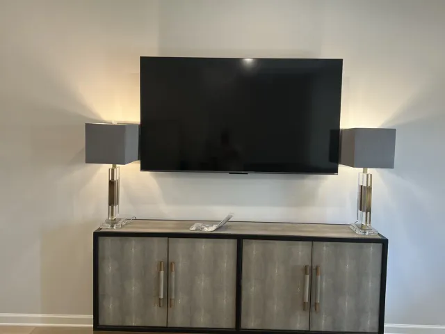A TV on a flat mount on a white wall above a gray console and a round gold table