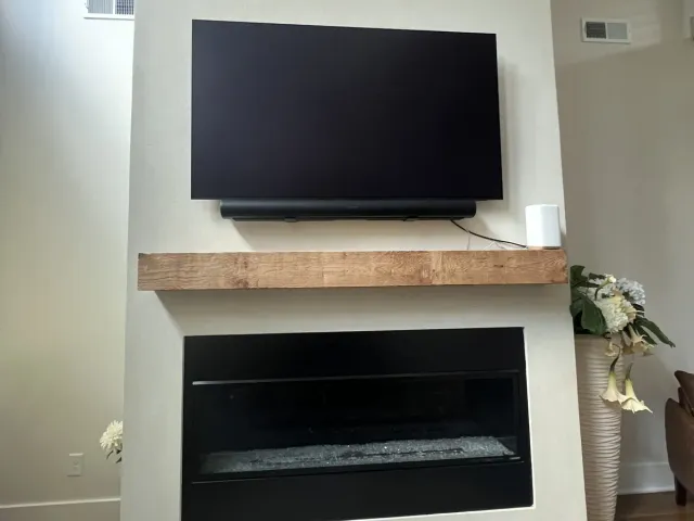 A TV and soundbar above a rustic wood mantel on a smooth white fireplace with a linear firebox