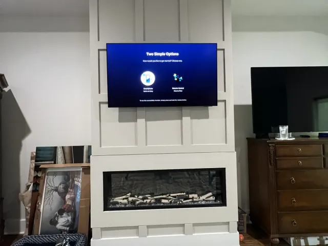 A TV mounted on a board-and-batten fireplace wall above a linear electric fireplace, next to a wood dresser