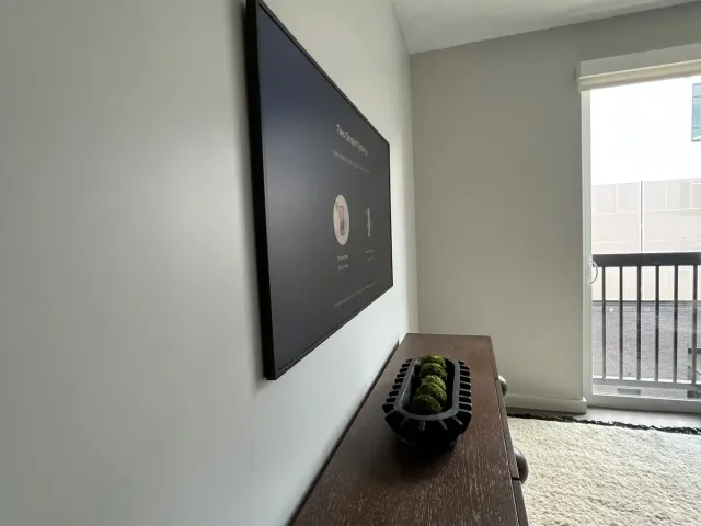 A TV on a flat mount on a white wall beside a dark wood console