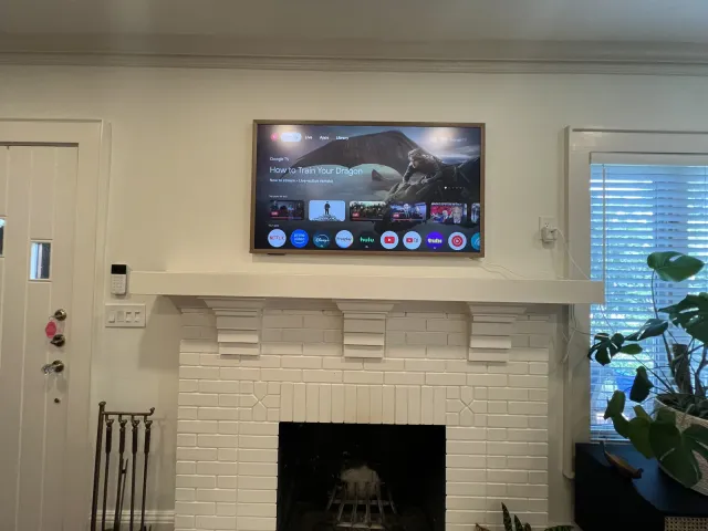 A TV mounted above a white mantel on a white painted-brick fireplace in a cottage living room