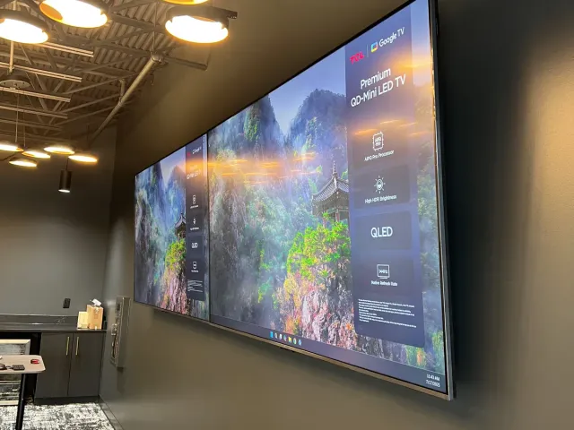 A large TV mounted high on a dark wall in a bar area under pendant lights