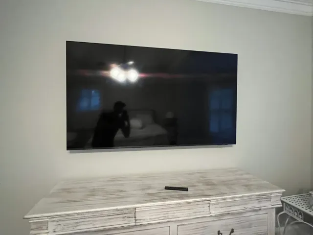 A TV on a flat mount on a gray wall next to a whitewashed dresser