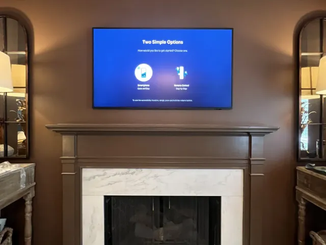 A TV mounted on a brown wall above a dark wood mantel and white marble fireplace, mirrored niches on each side