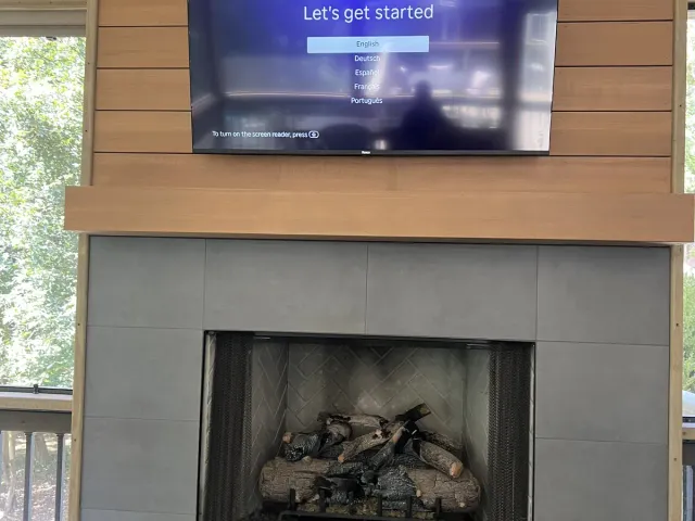 A Roku TV on a horizontal wood-plank chimney breast above a gray tile fireplace on a covered porch