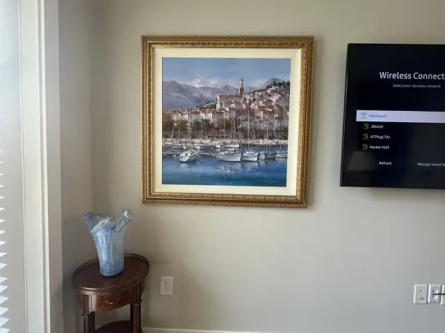 A TV mounted high on a bedroom wall above a framed painting