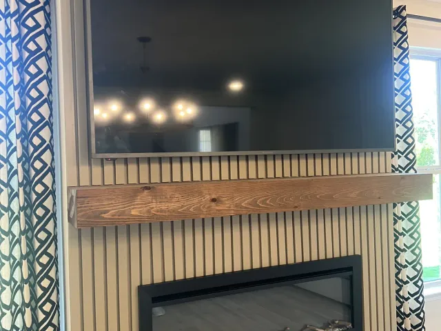 A TV on a vertical slat accent wall above a wood beam mantel and a linear electric fireplace