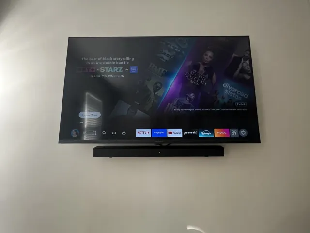 A TV with a soundbar below it on a white bedroom wall beside a closet