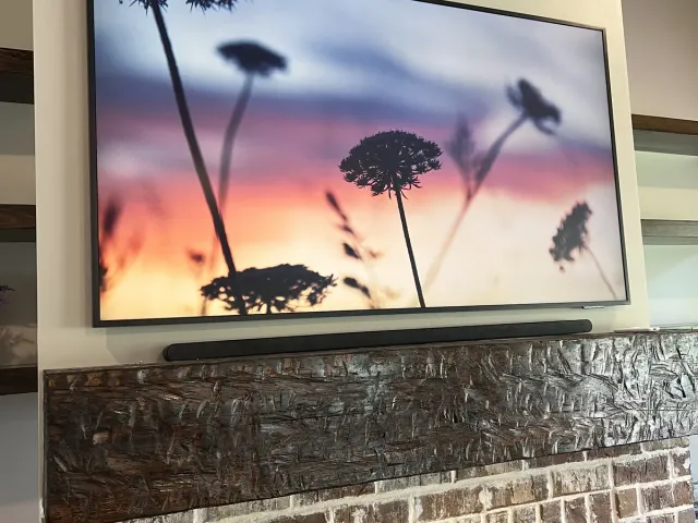 A Samsung Frame TV in Art Mode with a soundbar beneath it above a rustic brick fireplace with a dark wood mantel
