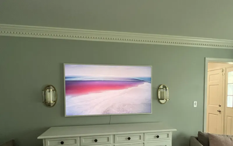A Frame-style TV showing artwork above a white dresser, its thin cable visible below the screen