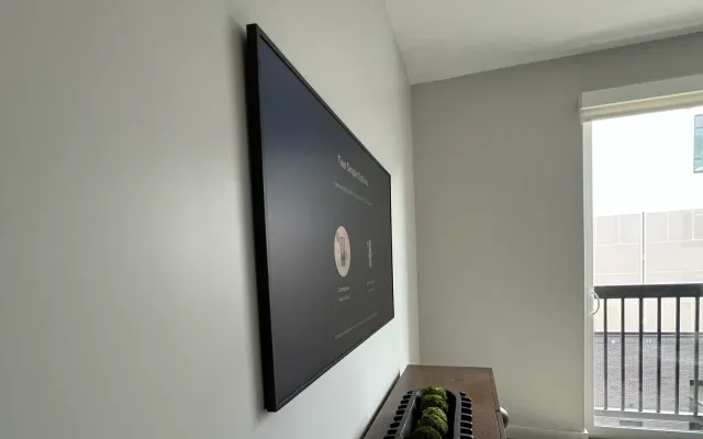 A TV mounted flat to a white wall in an apartment beside a balcony door